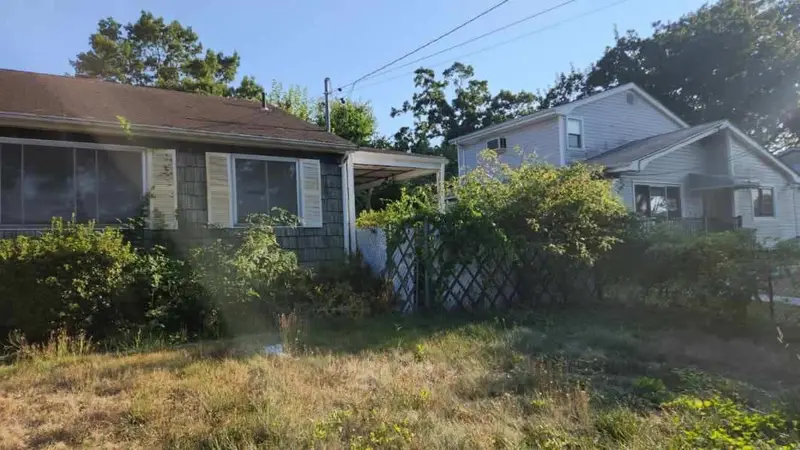 Ranch behind an overgrown front lawn and hedges, Brentwood, NY