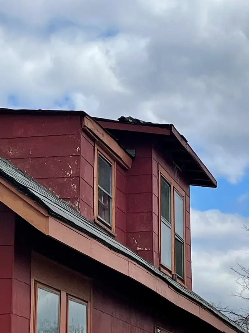 Red-sided dormer with weathered trim against a cloudy sky, Brentwood, NY